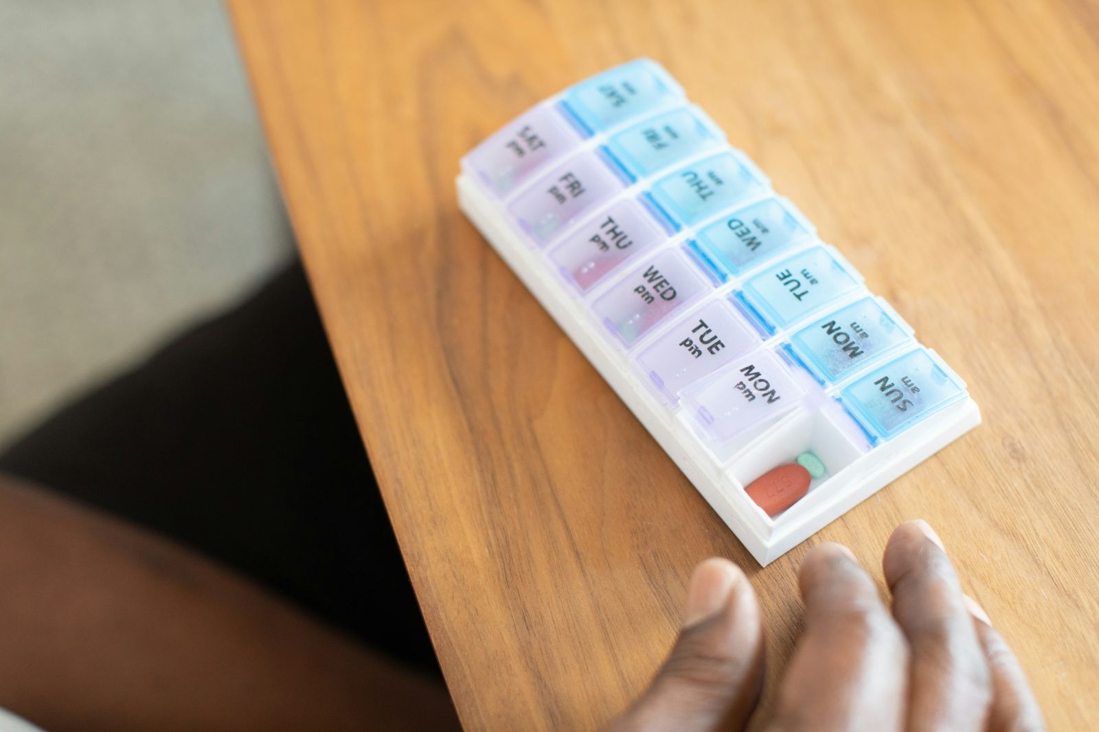 Weekly pill organiser with labelled day compartments on a wooden table